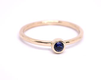 May include: A simple gold band ring with a single, round, bezel-set sapphire gemstone.