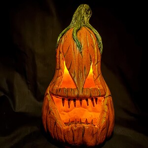 May include: A carved orange pumpkin with a menacing face, lit from within, creating a glowing effect. The pumpkin has a green stem and is a classic Halloween decoration.