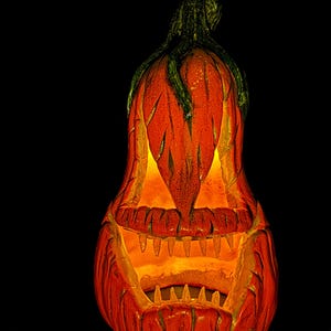 May include: A carved orange pumpkin with a menacing face, lit from within, against a black background. The pumpkin has sharp teeth and triangular eyes, with a green stem. A classic Halloween decoration.