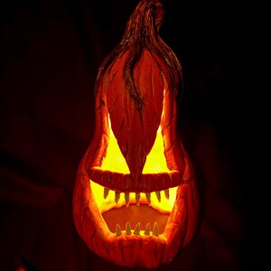 May include: A carved orange pumpkin with a glowing yellow interior, featuring triangular eyes and a jagged-tooth grin. The pumpkin's stem is dark brown, and the background is black, creating a spooky Halloween decoration.