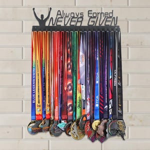 May include: A black metal medal display rack with the words "Always Earned NEVER GIVEN" above a row of colorful race medals. The medals have various ribbons and designs, showcasing achievements in sports and events.