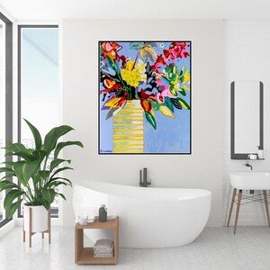 May include: A colorful abstract painting of a bouquet of flowers in a yellow vase against a light blue background. The painting is framed in black and hangs on a white wall in a bathroom.