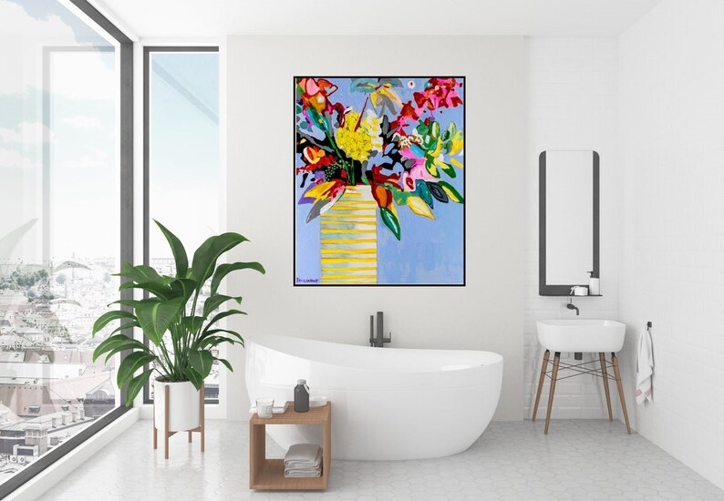 May include: A colorful abstract painting of a bouquet of flowers in a yellow vase against a light blue background. The painting is framed in black and hangs on a white wall in a bathroom.