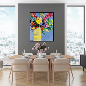 May include: A colorful abstract painting of a bouquet of flowers in a yellow vase against a blue background. The painting is framed in black and hangs on a gray wall in a dining room setting.