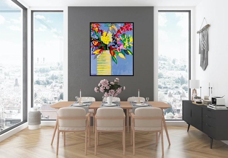 May include: A colorful abstract painting of a bouquet of flowers in a yellow vase against a blue background. The painting is framed in black and hangs on a gray wall in a dining room setting.