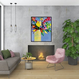 May include: A colorful abstract painting of a bouquet of flowers in a yellow vase against a blue background. The painting is framed and hanging on a wall in a living room setting.