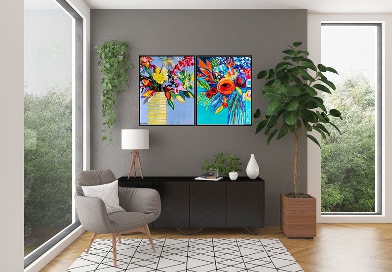 May include: Two framed abstract paintings of colorful flower arrangements. The paintings are hung on a gray wall above a black cabinet with a wooden top. A gray armchair with a white pillow sits in the corner of the room.