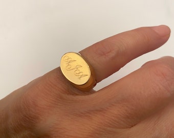 Könnte beinhalten: Ein goldener Siegelring mit einer ovalen Oberseite, die mit dem Namen "M.J.S.A." graviert ist.