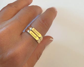 Könnte beinhalten: Zwei gestapelte Ringe aus goldfarbenem Metall mit flachen, rechteckigen Oberflächen. Der obere Ring ist mit dem Wort tenn in Schreibschrift graviert, der untere Ring mit dem Wort nash in einer passenden Schreibschriftart.