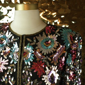 May include: A black sequined jacket with a gold zipper and colorful floral embroidery. The sequins are iridescent and create a shimmering effect.