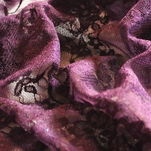 May include: Purple lace fabric with a delicate floral pattern. The fabric is soft and sheer, with a slightly shimmery finish.