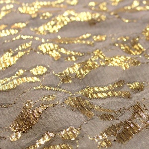 May include: Close-up of a beige fabric with a gold metallic floral pattern. The fabric has a textured surface and a subtle sheen.