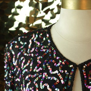 May include: A black sequined jacket with a colorful pattern of sequins. The jacket has a V-neck and a button closure.