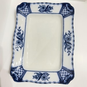 May include: Rectangular white ceramic serving platter with a blue floral and geometric border design. The platter has a slightly scalloped edge and features floral motifs at each corner and along the sides.