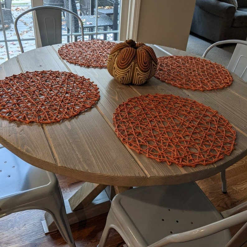 May include: A round wooden table with four chairs, set with four orange woven placemats and a decorative pumpkin in the centre.