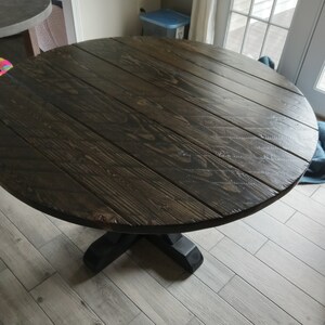 May include: A dark brown round table with a pedestal base. The table top has a wood grain pattern and is made of solid wood.