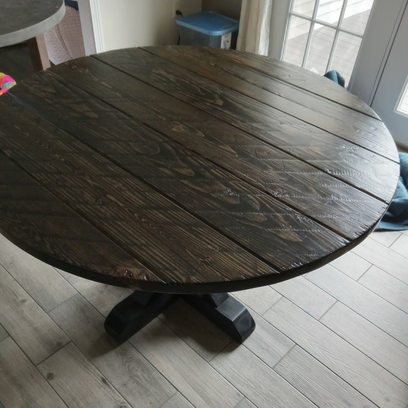 May include: A dark brown round table with a pedestal base. The table top has a wood grain pattern and is made of solid wood.