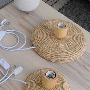 May include: Two round woven wicker lampshades with wooden bases and white electrical cords with inline switches. The lampshades are on a light wood table.