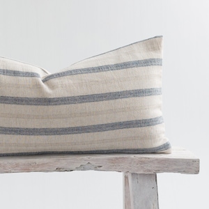 May include: A long, rectangular pillow with a white and blue striped pattern. The pillow is sitting on a white wooden bench.