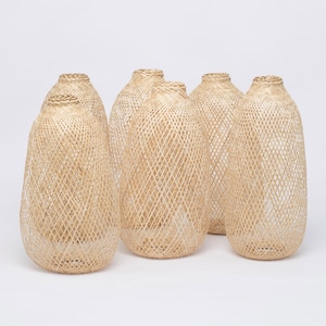 May include: Set of six woven wicker lampshades in a light beige color. The lampshades are oval shaped and have a diamond pattern.