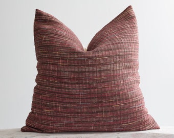 May include: A burgundy and brown striped throw pillow with a textured woven fabric. The pillow is sitting on a white wooden bench.
