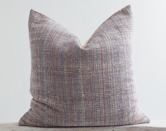 May include: A decorative throw pillow with a woven fabric cover in shades of blue, purple, and brown. The pillow is sitting on a white wooden bench.