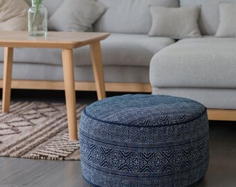 Puede incluir: Un puf redondo azul y blanco con estampado, con un sofá gris y una mesa de café de madera en el fondo.