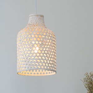 May include: A white woven pendant light fixture with a geometric pattern. The light is turned on and illuminates the room.