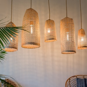 May include: Five woven wicker pendant lights hang from the ceiling, casting a warm glow on a white wall. The lights are all the same shape and size, and they are made of natural materials.