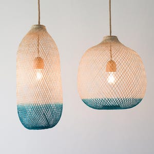 May include: Two woven pendant lights with a teal blue and natural color gradient. The lights are hanging from a white ceiling.