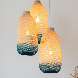 May include: Three woven pendant lights with a light brown and teal color scheme. The lights are hanging from the ceiling and are illuminated.