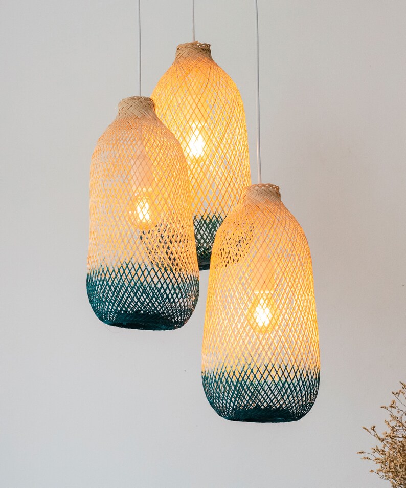 May include: Three woven pendant lights with a light brown and teal color scheme. The lights are hanging from the ceiling and are illuminated.