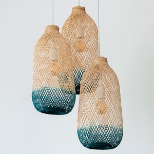 May include: Three woven pendant lights with a teal blue ombre effect. The lights are made of natural materials and have a rustic, bohemian style.