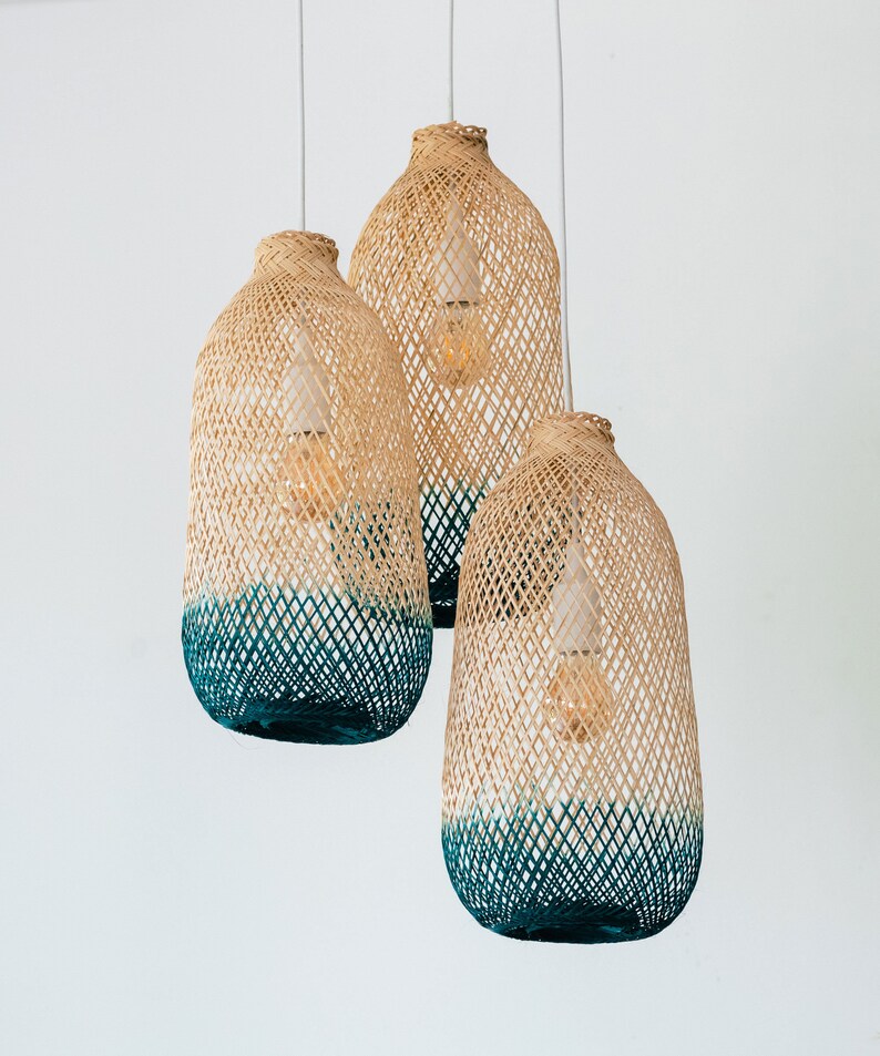May include: Three woven pendant lights with a teal blue ombre effect. The lights are made of natural materials and have a rustic, bohemian style.