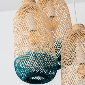 May include: Three woven pendant lights with a teal ombre effect. The lights are made of natural materials and have a rustic, bohemian style.