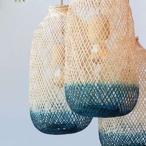 May include: Three woven bamboo pendant lights with a teal blue ombre dip dye effect. The lights are hanging from the ceiling and are illuminated with light bulbs.