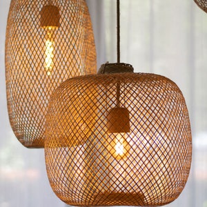 May include: Two woven rattan pendant lights with exposed light bulbs. The lamps have a warm, golden glow, and are suspended from the ceiling. The lampshades are a natural brown color and have a lattice design. The background is a soft, neutral color.