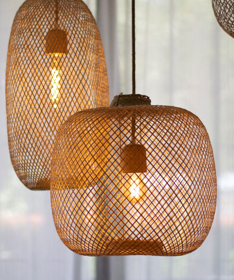 May include: Two woven rattan pendant lights with exposed light bulbs. The lamps have a warm, golden glow, and are suspended from the ceiling. The lampshades are a natural brown color and have a lattice design. The background is a soft, neutral color.