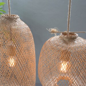 May include: Two woven bamboo pendant lights with exposed light bulbs. The lamps have a natural, light brown color and are suspended from the ceiling by rope. The lampshades have a diamond pattern.