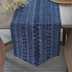 Puede incluir: Un camino de mesa azul y blanco con un diseño geométrico. El camino de mesa está hecho de algodón y tiene un borde con flecos.