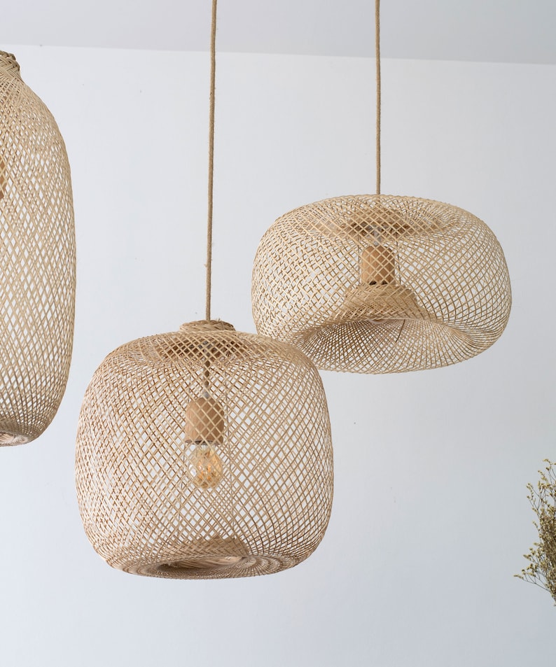 May include: Three woven rattan pendant lights hanging from the ceiling. The lampshades have a natural beige color and a lattice design. Each light fixture has a visible lightbulb inside, and they are suspended by a natural rope.