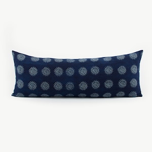 Puede incluir: Una almohada larga y rectangular de color azul con un patrón de sol blanco. La almohada está hecha de una tela suave y texturizada.