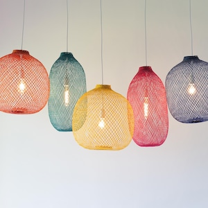 Può includere: Cinque lampade a sospensione colorate con un design a gabbia intrecciata. I paralumi sono nei toni dell'arancione, del verde acqua, del giallo, del rosa e del blu navy. Ogni lampada ha una singola lampadina visibile all'interno. Appese a sottili cavi argentati.