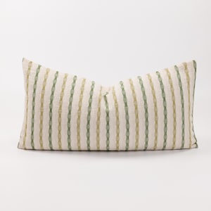 Puede incluir: Una almohada rectangular larga con fondo blanco y rayas verdes y amarillas. Las rayas están hechas de un patrón tejido.