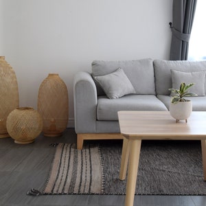 May include: A gray sofa with three pillows, a wooden coffee table, and three woven baskets in front of a white wall. A small potted plant sits on the coffee table.