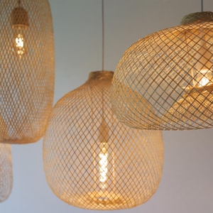 Pu&ograve; includere: Tre luci a sospensione intrecciate di colore marrone chiaro naturale. Le luci sono realizzate in un materiale intrecciato che crea un motivo geometrico. Le luci sono appese al soffitto e sono illuminate.