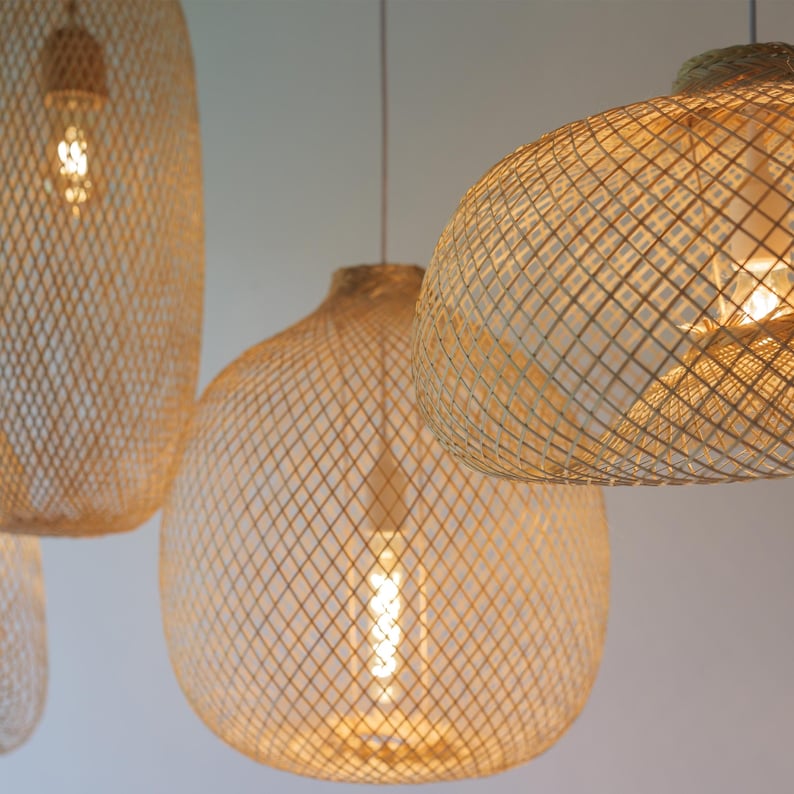 Pu&ograve; includere: Tre luci a sospensione intrecciate di colore marrone chiaro naturale. Le luci sono realizzate in un materiale intrecciato che crea un motivo geometrico. Le luci sono appese al soffitto e sono illuminate.