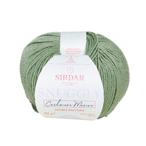 Puede incluir: Una madeja de lana verde salvia Sirdar Snuggly Cashmere Merino para tejido doble. La etiqueta indica 50 gramos y aproximadamente 130 metros. La lana es de un color verde suave, ideal para proyectos de punto y ganchillo.