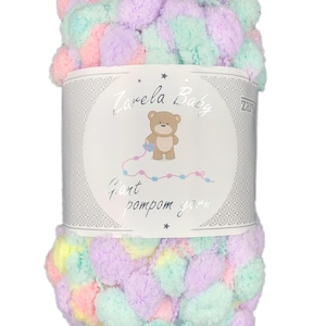 Op de afbeelding: Een bol pastelkleurig gigantisch pompon garen. Het garen is in tinten roze, paars en groen. Het label luidt "Zarela Baby Giant Pom Pom Yarn".