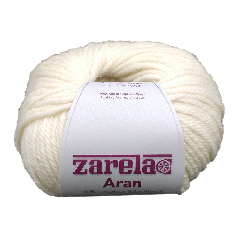 May include: A ball of white yarn labeled "zarela Aran 100% Luxurious Baby Alpaca". The label also includes the weight (50g), length (80m/87yd), and fiber content (100% Alpaca).